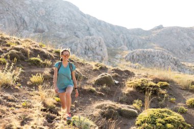 a young girl with a backpack walks along a mountain path. travel and freedom