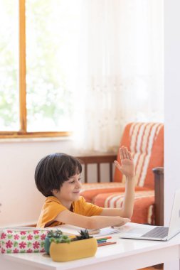 Çocuk internetten öğrenme dersinde elini kaldırıyor. Bilgisayarlı bir çocuk bir öğretmen ve sınıf grubuyla video konferans yoluyla iletişim kuruyor. Çocuk internetten iletişim kuruyor..