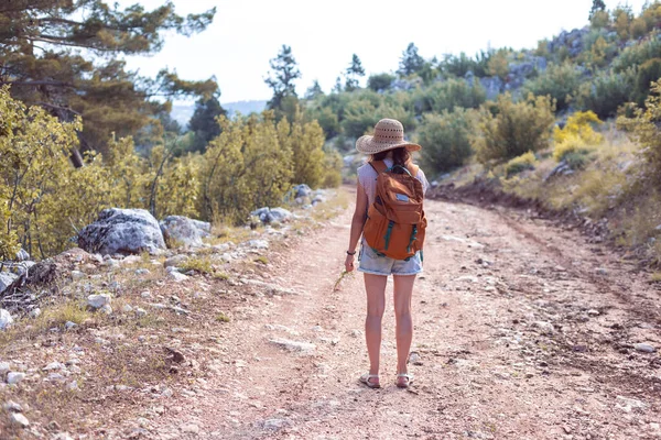 Portrait of a woman with a backpack and a straw hat in the forest, a smiling girl on a hike, summer trekking, happy woman enjoying her walk on a mountain path