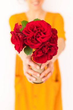 Kız elinde kırmızı güller tutuyor, kadın elinde bir vazo çiçek tutuyor, kız bir buket veriyor.