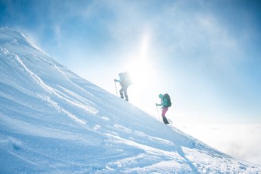 climbing a snow-covered mountain during a snow storm, two women in winter trekking, climbers climb to the top of the mountain in winter
