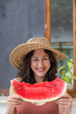 Hasır şapkalı gülen kız karpuz yiyor, elinde karpuz dilimi tutan kadın