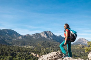 Sırt çantalı genç bir kadın dağın tepesine tırmandı ve vadiye baktı, dağlarda yürüyüş yaptı, hedefe ulaşmada başarılıydı.