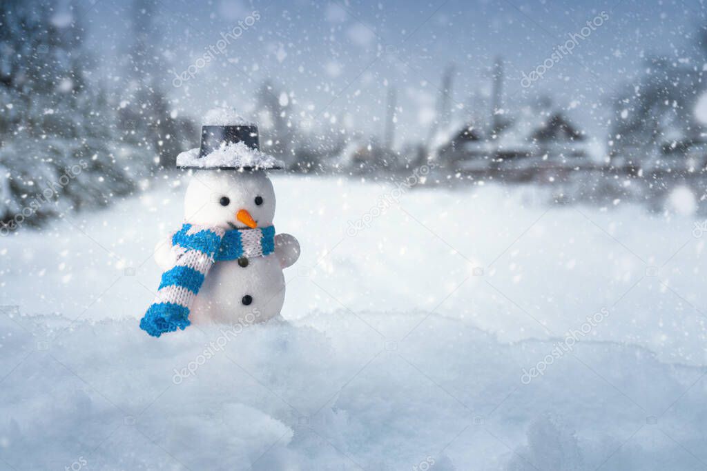 Funny snowman stands in the snowdrift with blurred houses of a village on the background in snowy winter evening