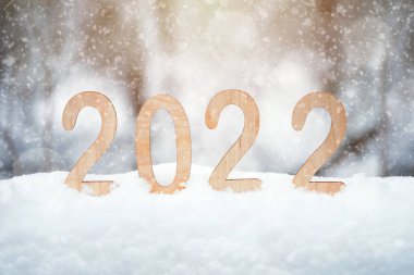 2022 kontrplak yeni yıl rakamları kar taneleri ve güneş ışınlarıyla kış ormanlarında bir kar yığınının içinde duruyor. Sığ alan derinliği.
