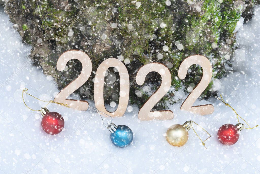 2022 wooden new year figures on the snow with christmas balls leaning against the tree trunk outdoors in winter forest