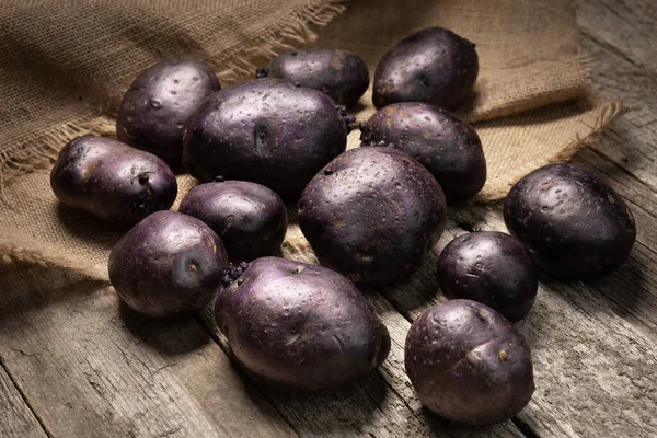 Raw violet vitelotte potatoes on wooden boards and burlap cloth — Stock Photo, Image
