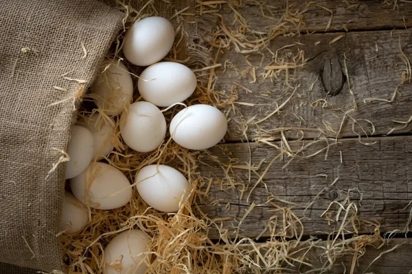 Weiße Hühnereier gerollt aus dem Kleesack auf Holzbrettern mit Stroh — Stockfoto