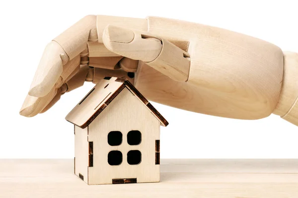 Verzekeringsconcept. Houten poppen hand bedekt een houten speelgoedhuis geïsoleerd op wit. — Stockfoto