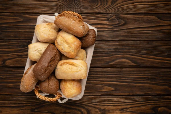 Fresh wheat and rye bread in a wicker basket on a brown wooden table — Stock Photo, Image