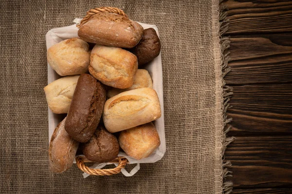 Chleb pszenny i żytni w wiklinowym koszu na tkaninie na brązowym drewnianym stole — Zdjęcie stockowe