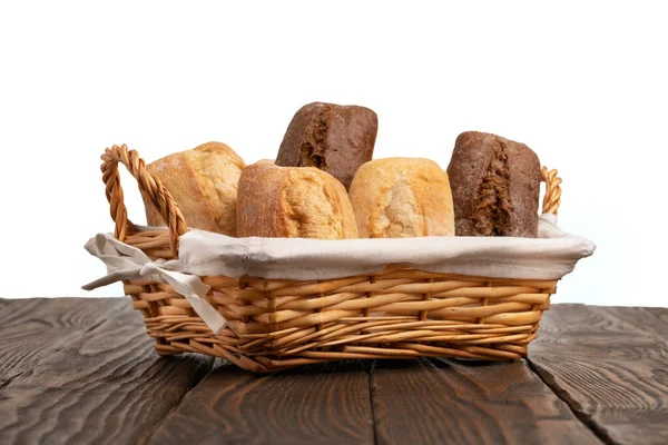 Wicker basket full of fresh wheat and rye buns on a brown wooden table isolated on white — Stock Photo, Image