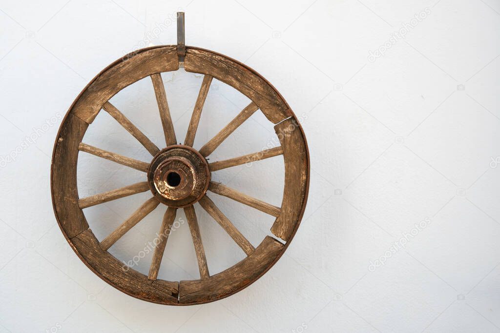 Vintage wooden cartwheel hangs on a white cement wall. Copy space