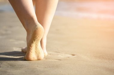 Sıcak güneşli bir günde, bir sahil şeridinin yakınındaki deniz kumu üzerinde çıplak ayaklarıyla...