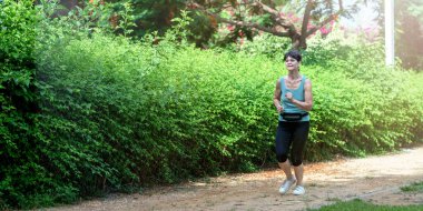 Mature caucasian woman running along a path in the park in summer morning in Israel