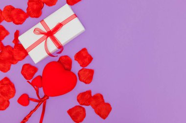 Mor bir arka planda birkaç kırmızı taç yaprakları vardır, beyaz bir kağıda sarılmış bir hediye ve bir fiyonklu bir kurdele ve bir sopaya bağlı üç kalp. Bir tarafta bir sürü kopya alanı var..