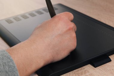 Elektronik kalemle grafiksel tabletle çizen bilinmeyen bir adamın eli. Düğmeler tabletin solunda görünür..