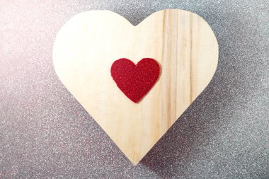 Gümüş parıltılı bir yüzeyde tahta bir kalp vardır. Üstünde de daha küçük, kırmızı bir kalp..