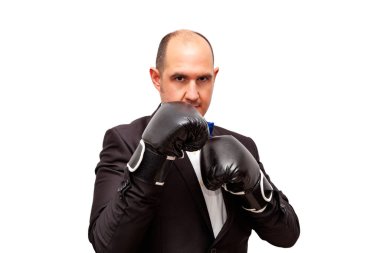 A bald adult Caucasian male dressed in a suit, shirt and bow tie is wearing black boxing gloves and is in a fighting stance. The background is white.