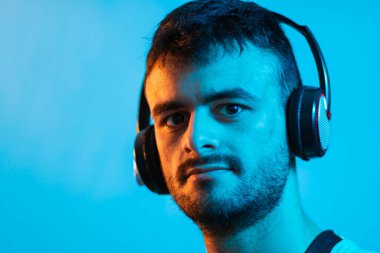 Müzik dinlemek için kulaklık takan beyaz sakallı genç bir adamın portresi. Mavi ve turuncu renkli ışıklarla aydınlatılır..