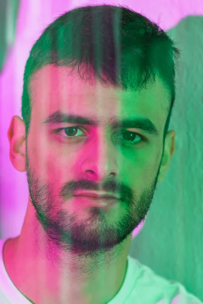 Sakallı genç bir beyaz adamın portresi aynanın arkasında yansımalar görülebilir. Yeşil ve morumsu ışıklarla aydınlatılır..