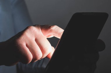 Bilinmeyen bir beyaz adamın cep telefonunun ekranına dokunurken yakın plan. Aygıttan gelen ışığın olduğu karanlık bir yerde..