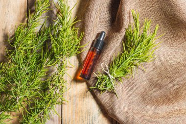 Yukarıdan bakıldığında, bazı ahşap tahtaların üzerinde kahverengi cam bir şişe var. İçinde gerekli yağ ile kaplanmış siyah bir durdurucu ve damlatıcısı var. Etrafında bir çuval bezi ve biberiye dalları vardır..