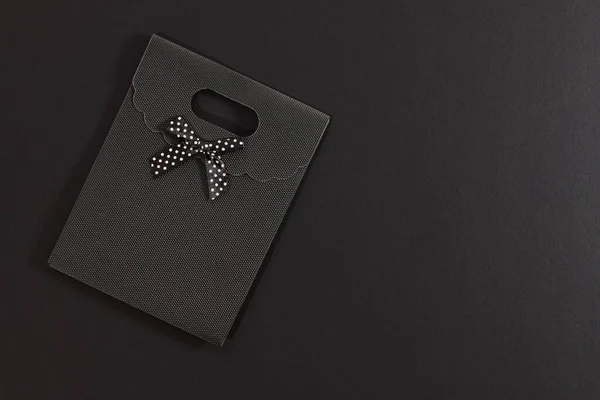 Black gift envelope with polka dot bow isolated on dark background. On one side there is empty space.