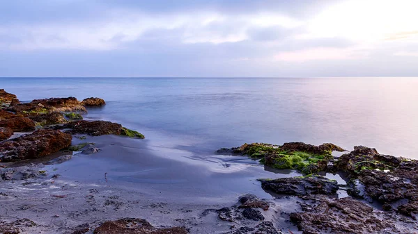 海岸上有一个沙滩 岩石和绿色海藻的海景 长期的暴露对海水和云彩产生了丝状的影响 天空乌云密布 色调蔚蓝 — 图库照片
