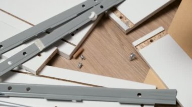 Evde mobilya montajı. Çekmece parçaları ve parçaları yığını yerde yatıyor. Sürgüler, vidalar, vidalar, perdeler ve bağlayıcılar düşüyor.