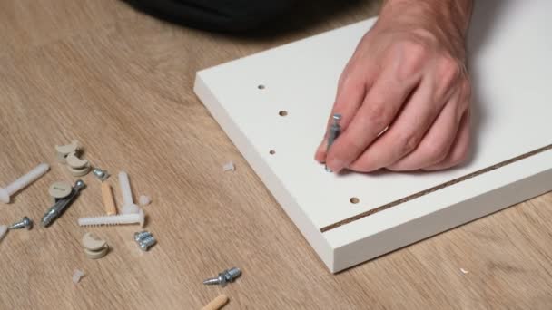 Caucasian man drives two bolts or lag screws with electric powered drill into white wooden board. Assembling furniture with screw gun at home — Stock Video