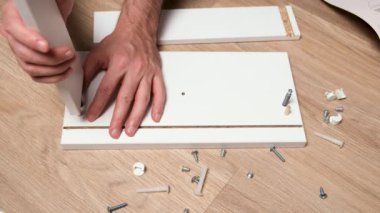 Evde mobilya montajı. Kafkasyalı adam çekmeceleri ahşap perdeler ve vidalarla birleştiriyor. Yerde bir yığın cıvata ve bağlayıcı var.