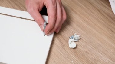 Beyaz adam altıgen vida sürücüsünü elektrikli matkapla ya da beyaz tahta tahtaya vida tabancasıyla kullanıyor. Evde vidayla mobilya monte etmek. Kapat.