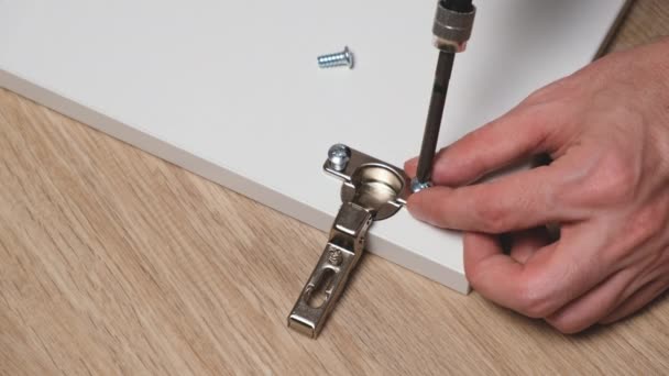 Assembling furniture at home. Caucasian man attaching hinge plate to white wooden door. Driving lag screw with electric powered drill or screw gun, close-up — Stock Video