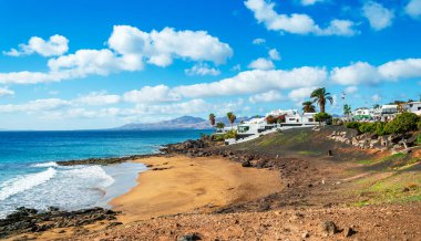 Lanzarote, Puerto del Carmen 'deki Playa El Barranquillo plajı manzarası. Turkuvaz okyanus dalgaları, beyaz evler ve dağlar, Kanarya Adaları, İspanya