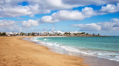 Lanzarote, Puerto del Carmen kasabasındaki Playa de los Pocillos plajı manzarası. Turkuaz okyanus suyuyla kumlu sahil manzarası, Kanarya Adaları, İspanya 'da turizm merkezinin beyaz evleri.