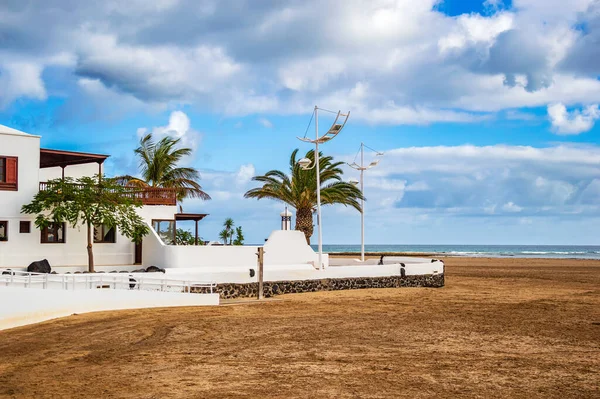 Casas brancas típicas na praia de Playa Honda na ilha Lanzarote, Espanha. Casa de férias perto do mar com palmeiras e praia de areia sob o céu azul nas Ilhas Canárias — Fotografia de Stock