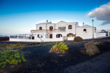 Typical canarian white houses on Lanzarote island, Spain. Beautiful traditional home on black vulcanic terrain with rare vegetation near ocean under blue sky