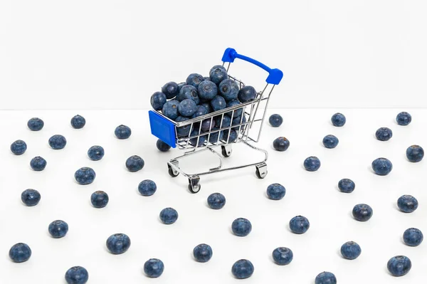 Blueberries in shopping cart and scattered berries isolated on white background. Shopping for healthy diet and natural vitamin food — Stock fotografie