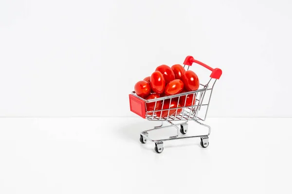 Cherry or roma tomatoes in red shopping cart isolated on white background. Shopping for vegetables and berries, healthy diet and natural vitamin food — Stock fotografie