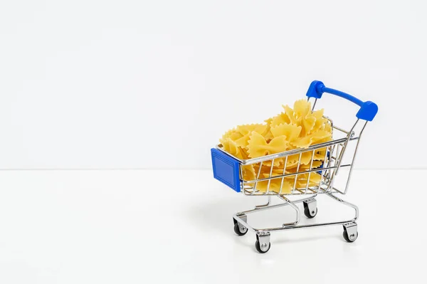 Farfalle pasta in blue shopping cart isolated on white background with copyspace for text. Food and groceries shopping, price increase, food crisis concept — Stock fotografie