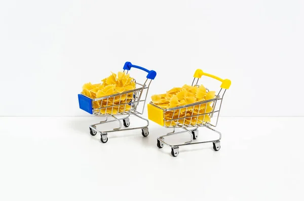 Uncooked farfalle pasta in blue and yellow shopping carts in colors of Ukrainian flag isolated on white background. Food supply crisis, price increase for wheat products, groceries shopping concept — Stock fotografie
