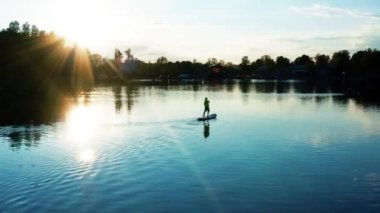 Aktif turizm ve sörf. Gün batımında göl kenarındaki yemek masasında gayet sağlıklı bir adamın insansız hava aracı görüntüsü. Yaz tatilinde su sporu yapan erkek silueti