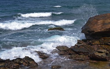 Kayalık sahilden denize su sıçraması ve beyaz deniz köpüğüyle bak.