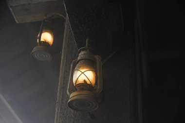 İçinde parlayan elektrik ampulleri olan iki antika fener karanlık bir duvara asılmış.