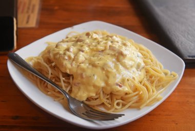 Ahşap bir masada beyaz bir tabakta kremalı soslu spagetti.