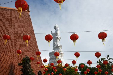 Vietnam tapınağında gökyüzüne karşı asılı bir Buda heykeli, ön planda Çin bayramı fenerleri asılı.