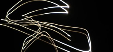 Neon Beyaz Dalga desenleri soyut bir şekilde izole edilmiş siyah bir arkaplanda akıyor. Uzun pozlama adı verilen ışık fotoğraf tekniği kullanılarak yapılmış. Eğri