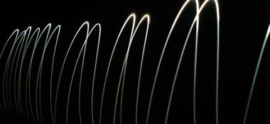 Neon Beyaz Dalga desenleri soyut bir şekilde izole edilmiş siyah bir arkaplanda akıyor. Uzun pozlama adı verilen ışık fotoğraf tekniği kullanılarak yapılmış. Eğri