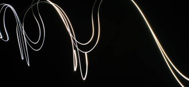Neon Beyaz Dalga desenleri soyut bir şekilde izole edilmiş siyah bir arkaplanda akıyor. Uzun pozlama adı verilen ışık fotoğraf tekniği kullanılarak yapılmış. Eğri